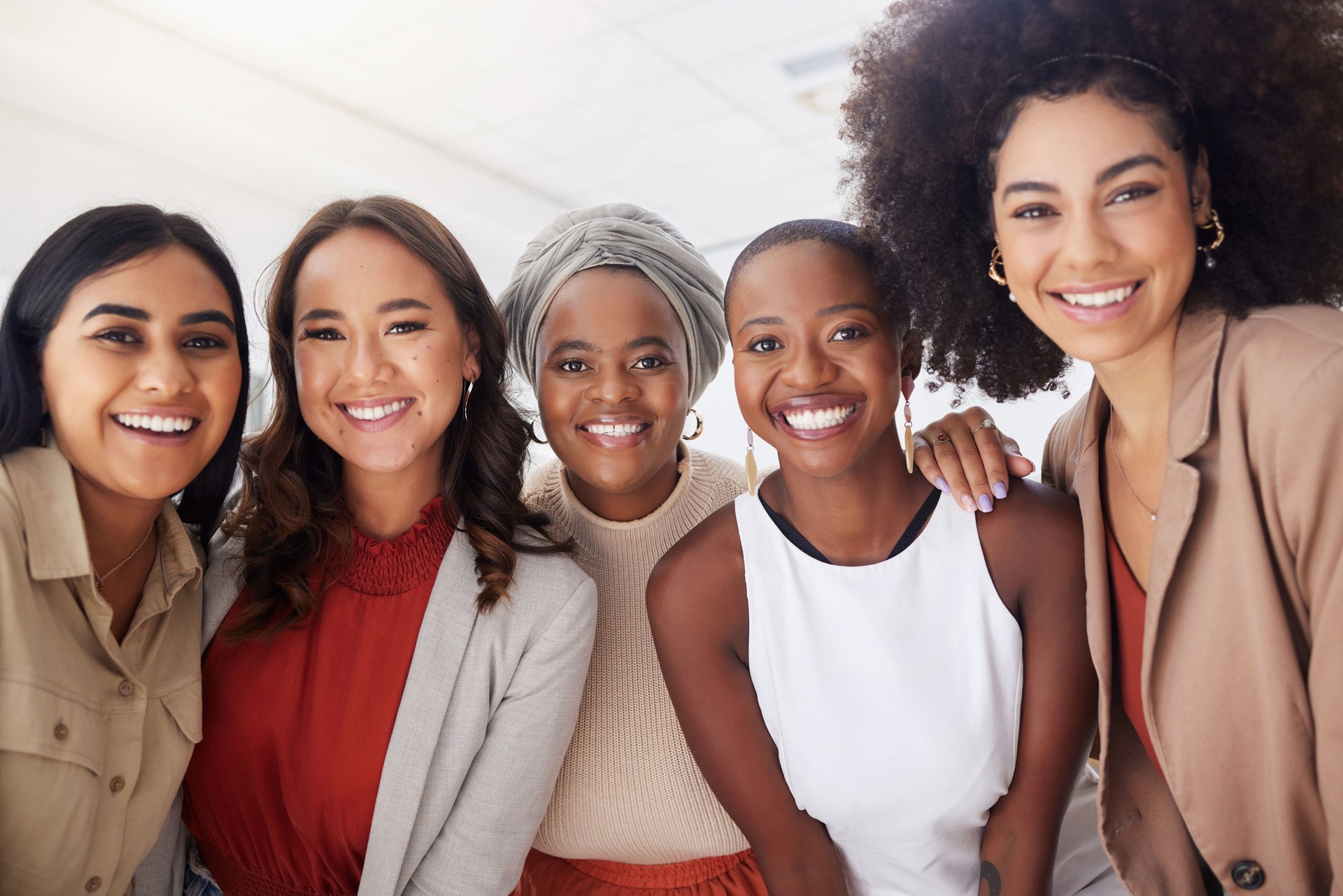 Portrait of a diverse group of smiling ethnic business women standing together in the office. Ambitious happy confident professional team of colleagues embracing while feeling supported and empowered