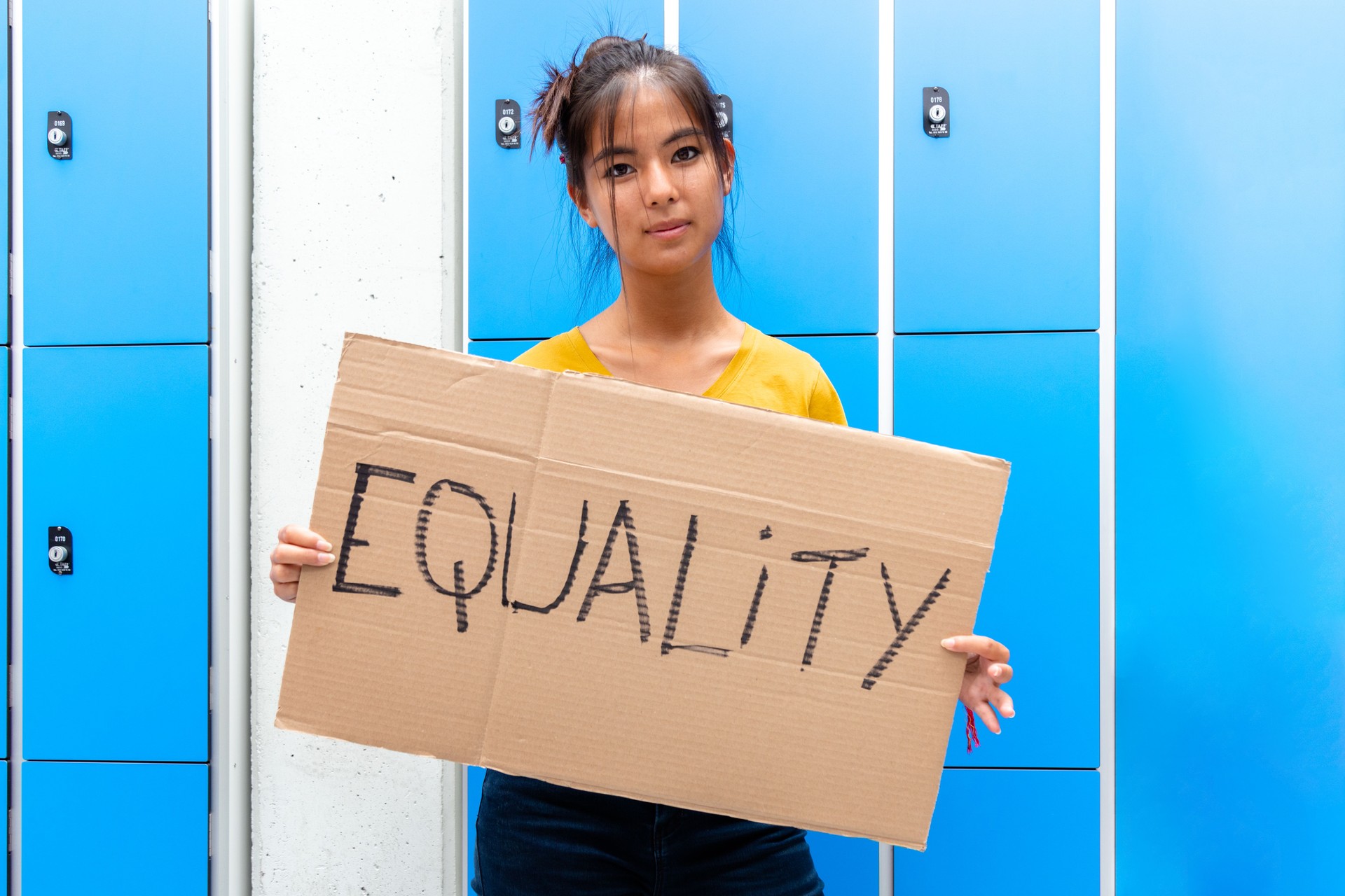 Teen asian girl looking at camera carrying an vindictive equality sign banner in high school.